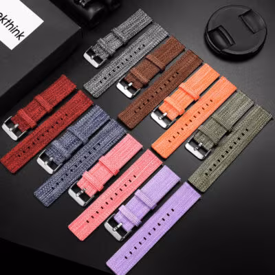 Overhead view of multiple quick release woven nylon watch bands in a range of colors: red, grey, black, pink, purple, green, orange, and brown, each with a stainless steel buckle.