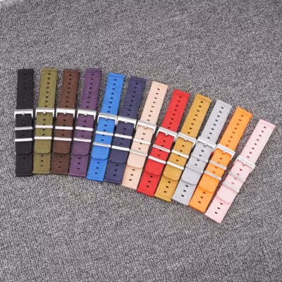 A diverse collection of twelve two-piece quick-release nylon watch straps in a wide range of colors (black, olive, brown, purple, various blues, beige, red, yellow, grey, orange, pink), fanned out on a grey textured surface.