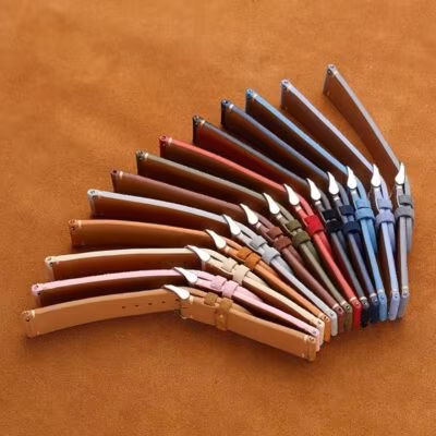 A fan arrangement of ten multi-colored suede watch bands showing their side profiles, soft leather linings, and the metal quick-release spring bar levers.